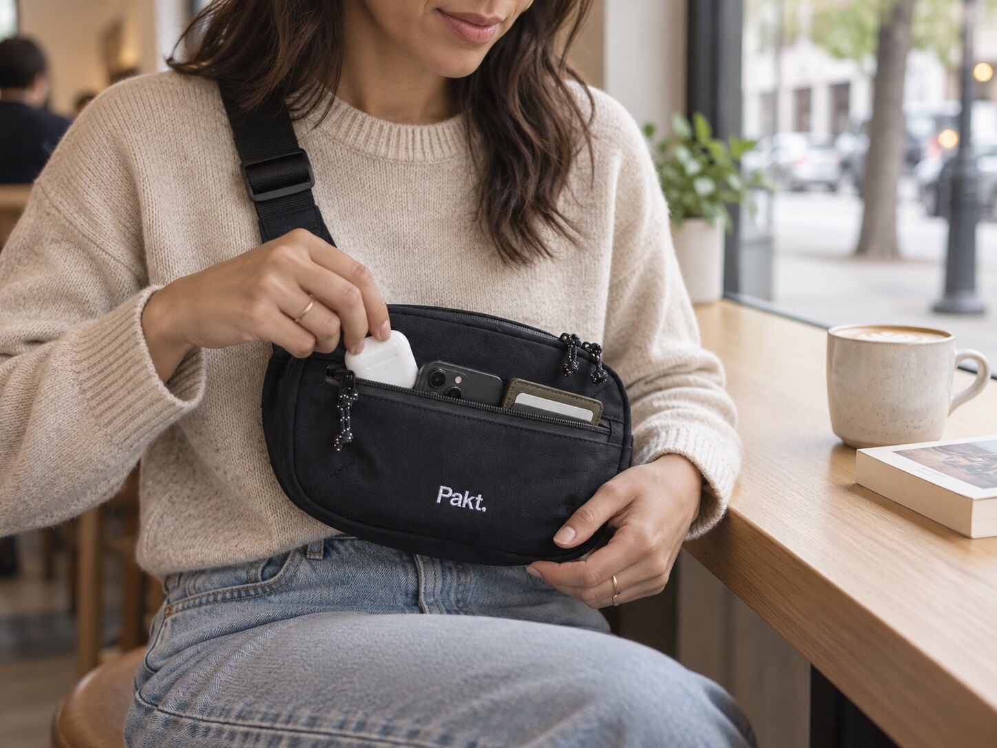 Earbuds, phone, and wallet organized in the black Pakt sling