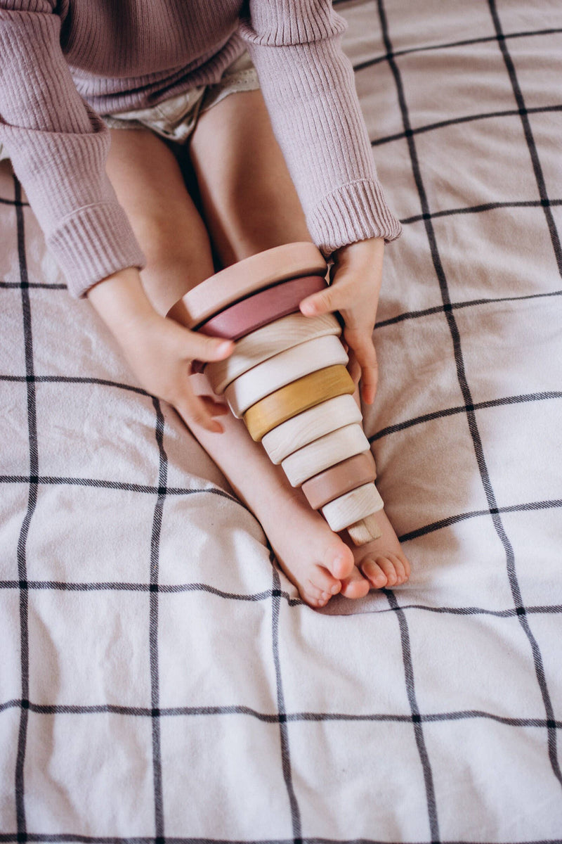 Child holding the SABO wooden ring stacker on a checked blanket