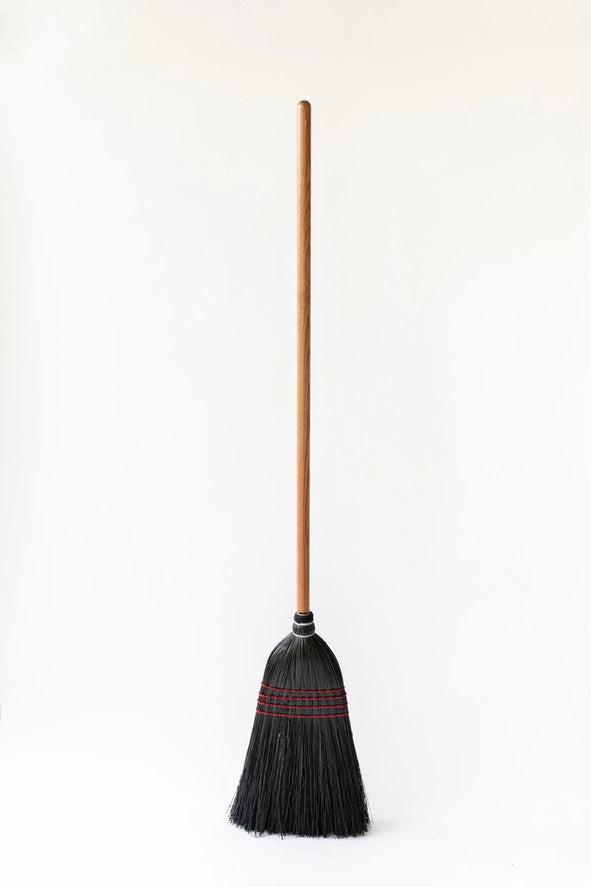 The Black Everyday Broom with black broom corn, four red-pink stitched bands, pale shoulder rings, and a solid oak handle