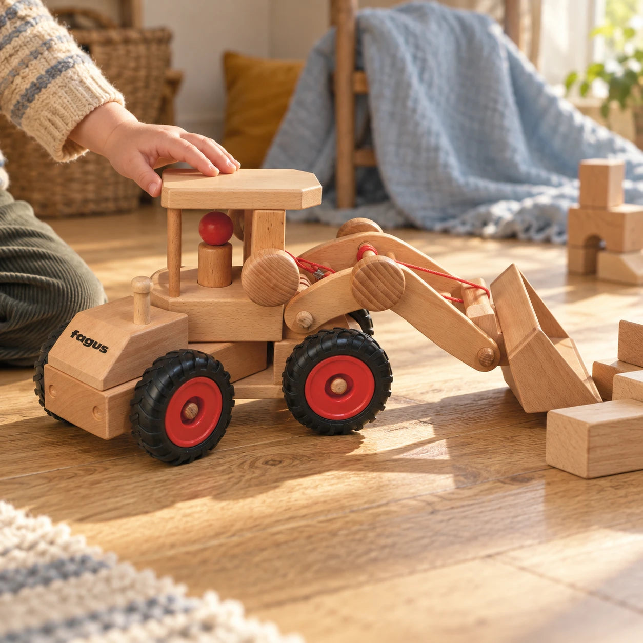 A child's hand guiding the Fagus Wheel Loader beside wooden blocks