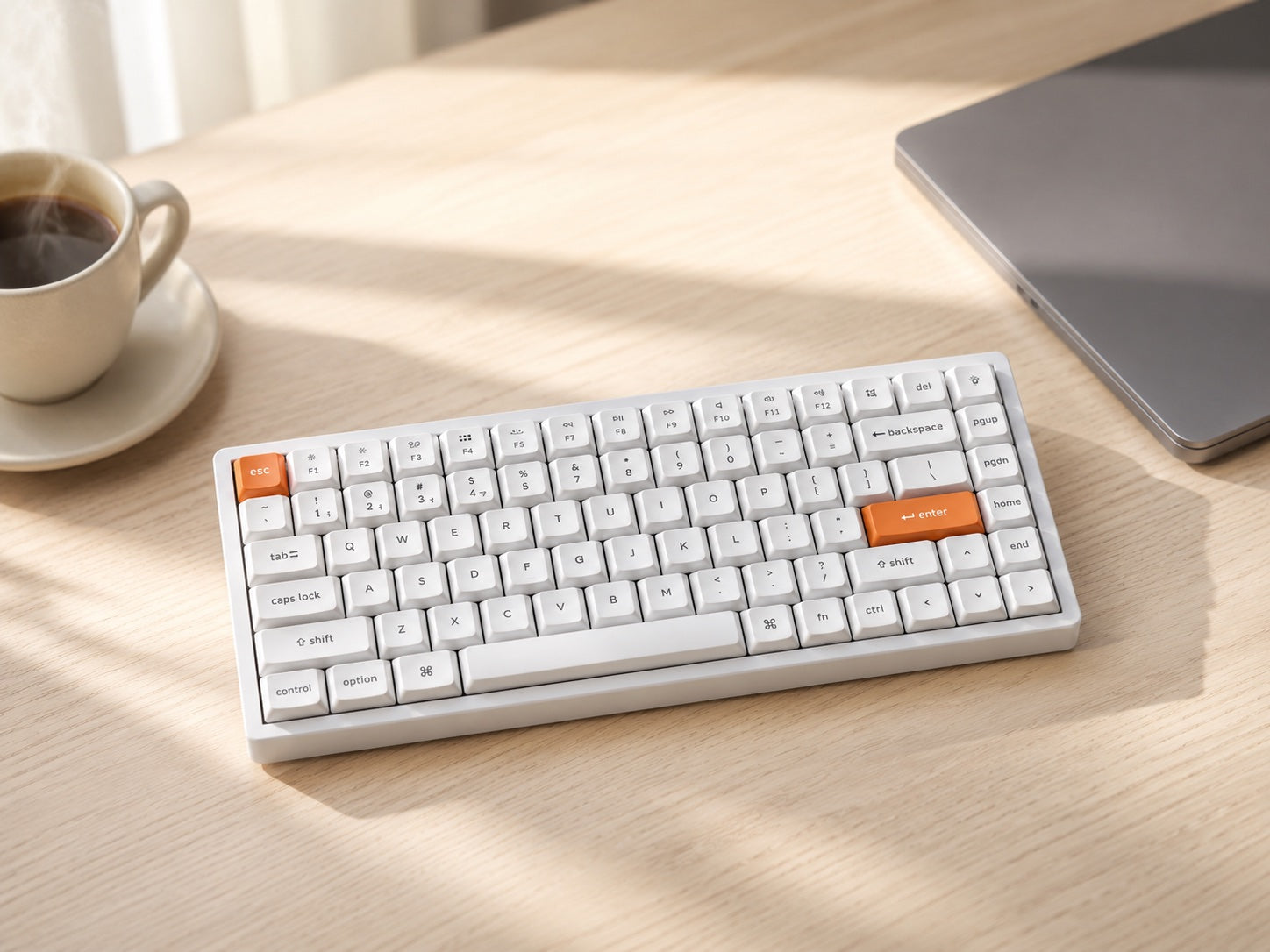 The white Keychron K2 Max on a bright desk beside a laptop and a coffee cup.