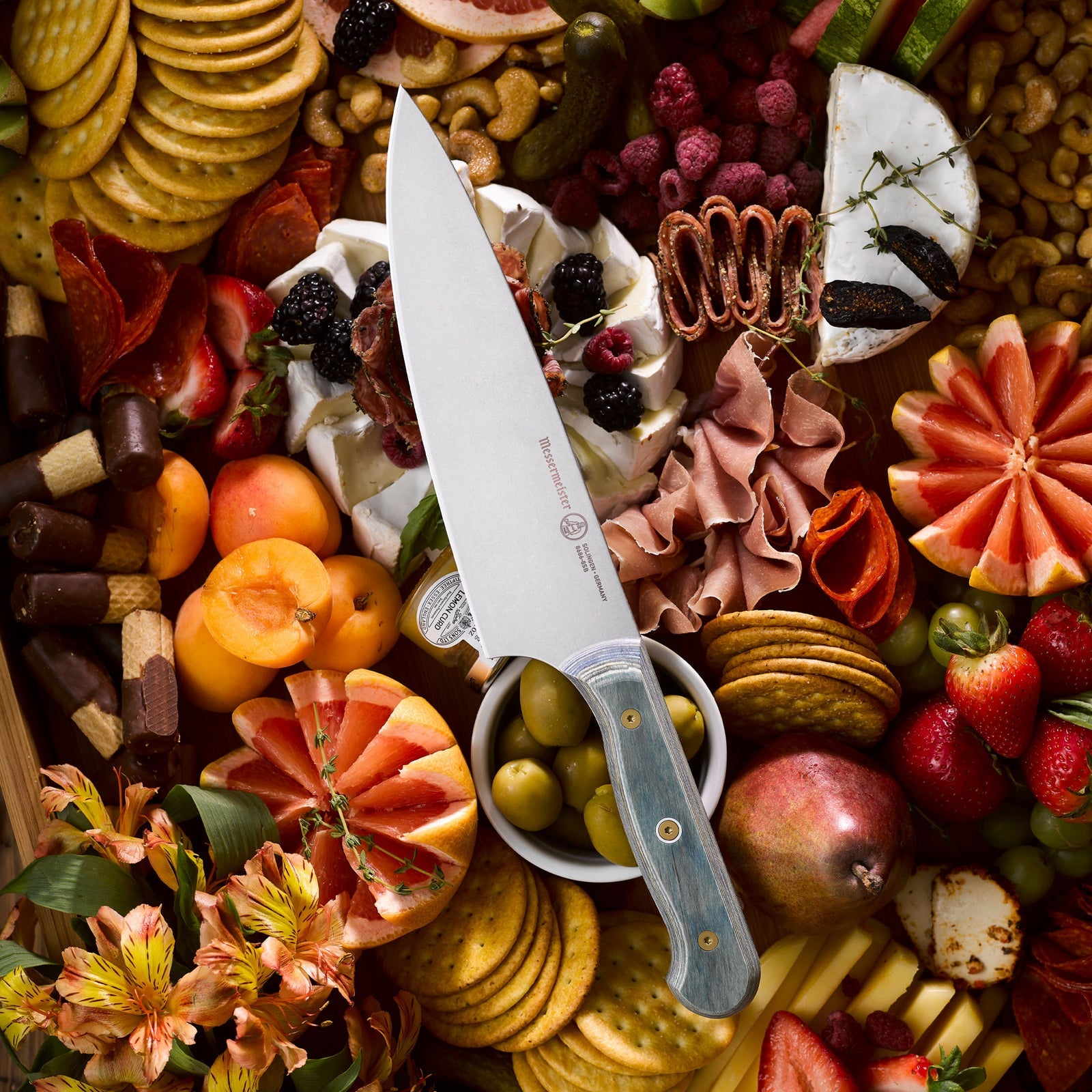 Custom Blue chef's knife arranged with fruit, cheese, and charcuterie